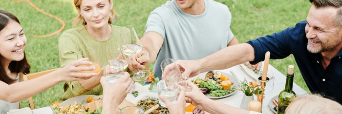 Gruppe von Freunden beim Anstoßen mit verschiedenen Getränken, darunter "0,0 % Alkohol" und alkoholfreie Optionen, während einer Mahlzeit im Freien