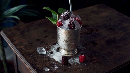 Ein klassischer Beeren-Cobbler in einem antiken Metallbecher, üppig garniert mit frischen Brombeeren, Himbeeren und zerkleinertem Eis