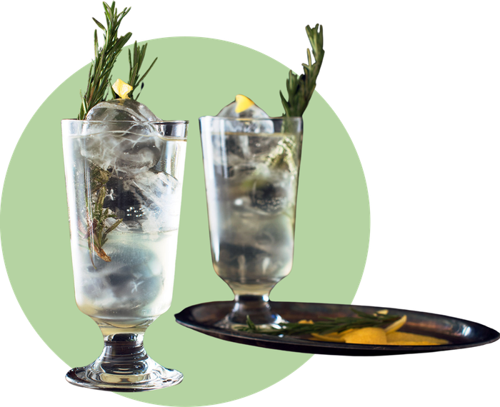 Zwei Gläser mit spritzigem Holunderblüten-Mocktail, verfeinert mit Rosmarinzweigen und Zitronenzeste, serviert auf einem eleganten Tablett