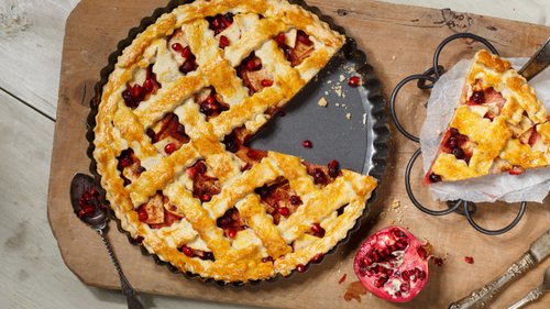 Ein goldbraun gebackener Granatapfelkuchen, ansprechend präsentiert auf einem Holzbrett mit einem Stück herausgeschnitten, bereit zum Servieren