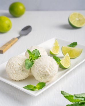 Drei Kugeln erfrischendes Sekt-Sorbet ohne Alkohol, serviert auf einer rechteckigen weißen Platte, garniert mit frischer Minze und Limettenspalten