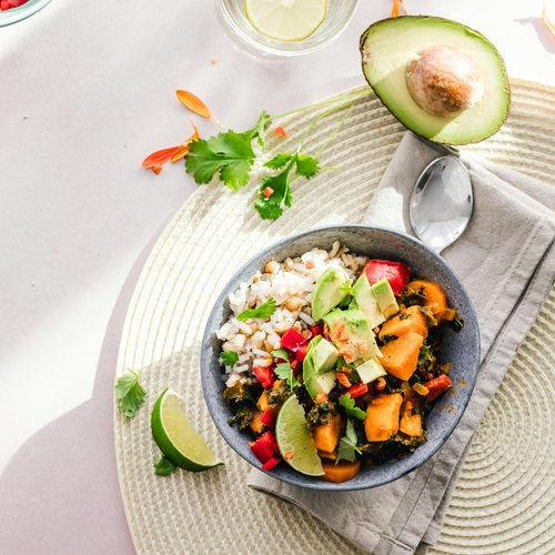 Zwei Schüsseln mit frischem Gemüsesalat, Avocado und Limettenscheiben auf einem hellen Tisch