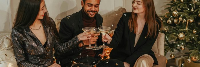 Drei Freunde stoßen mit alkoholfreien Getränken an einem festlich dekorierten Weihnachtsbaum an, um eine bewusste und alkoholfreie Silvesterfeier zu genießen.