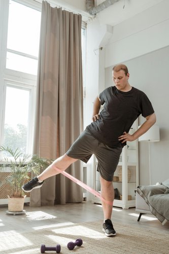 Mann macht Beintraining mit Widerstandsband in einem hellen Raum mit Pflanzen und Hanteln im Hintergrund