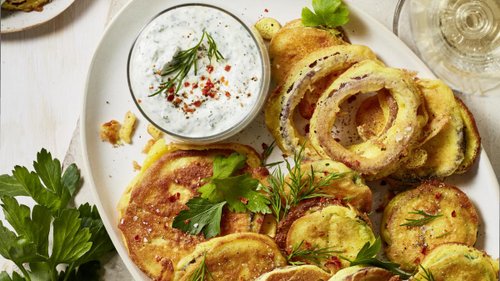 Appetitlich goldbraun frittiertes Gemüse im Rieslingteig, serviert auf einem weißen Teller mit einem cremigen Kräuter-Dip, garniert mit frischen Kräutern