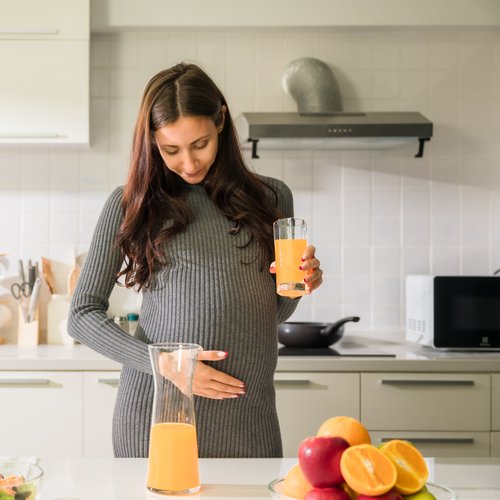 Schwangere Frau genießt frisch gepressten Saft in der Küche