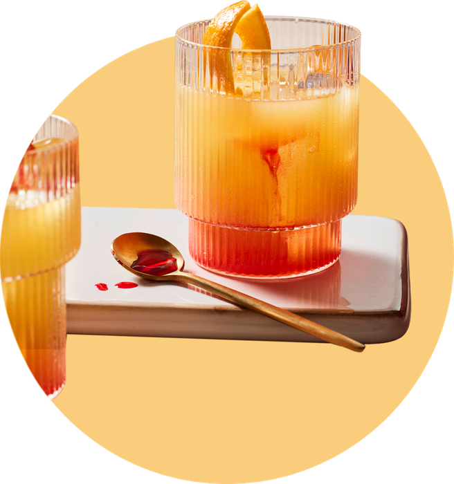 Zwei Orange Sour Cocktails mit eindrucksvollem Farbverlauf von Orange zu Rot, garniert mit Orangenscheiben, präsentiert auf einer modernen Marmorplatte