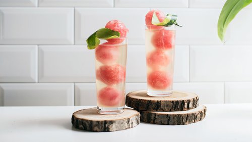 Erfrischende Wassermelonen-Ingwer-Mocktails mit gefrorenen Wassermelonenkugeln und einem Hauch von Ingwer, dekoriert mit Limettenschalen auf rustikalen Holzscheiben