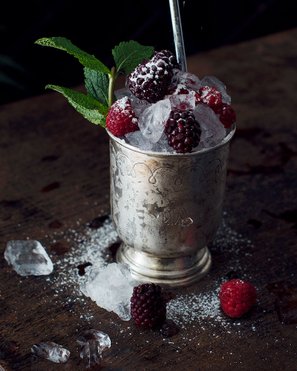 Ein klassischer Beeren-Cobbler in einem antiken Metallbecher, üppig garniert mit frischen Brombeeren, Himbeeren und zerkleinertem Eis