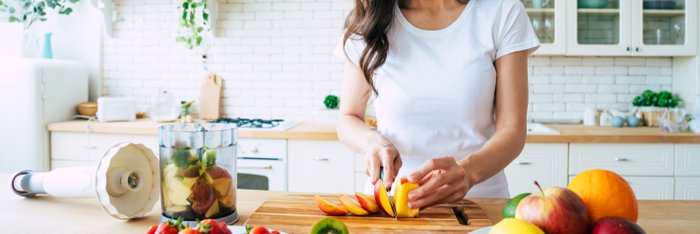 Lächelnde Frau bereitet in ihrer Küche einen frischen Obstsalat zu, eine gesunde Alternative zu kalorienreichen alkoholischen Getränken