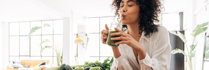 Eine Person genießt einen frischen grünen Smoothie neben einer Schale mit gesunden Zutaten in einem hellen Wohnraum, um den Lebensstil während des Dry January zu veranschaulichen.