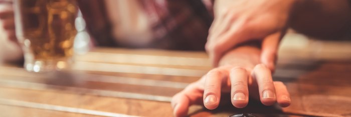 Hand einer Person, die neben einem Glas Bier und Autoschlüsseln auf einem Holztisch liegt, symbolisiert die Wichtigkeit der Entscheidung gegen Alkohol am Steuer auf der Informationsseite zum Thema "Alkohol am Steuer"